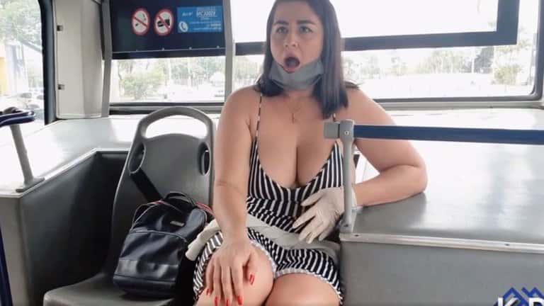 La mujer permanece sentada en la parte de atrás del bus mientras parece haber otros pasajeros en los demás asientos.